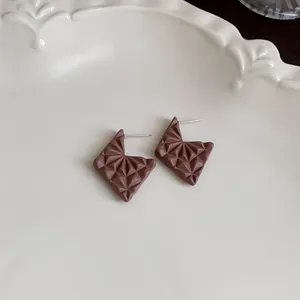 Close-up of Maillard coffee brown geometric stud earrings with 3D texture on a plate.