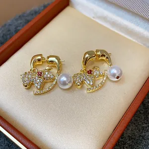 Close-up of gold-plated rocking horse earrings with sparkling stones and white pearls