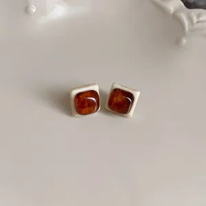 Macro view of vintage coffee square stud earrings with cream border on a ceramic plate.