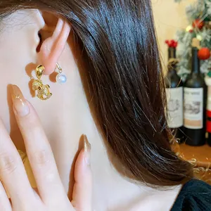 Close-up view of elegant gold horse-shaped earrings with a white pearl on a model.