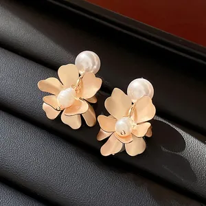 Detailed view of elegant golden flower earrings with glossy pearls on black leather.