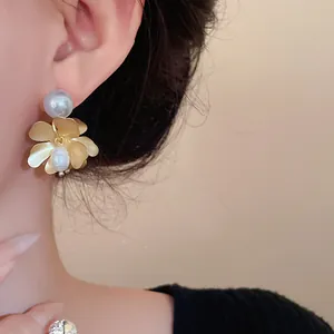 Close-up detail of elegant golden flower earrings with freshwater pearls and silver needles.