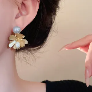 Elegant matte gold flower earrings with white freshwater pearls worn by a model ear.