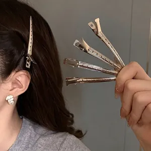 Minimalist silver metal duckbill hair clips shown on hair and held in a hand display