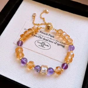 Primo piano di un bracciale con perle viola e gialle e catena dorata in scatola regalo