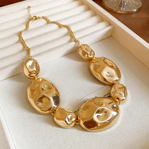 Chunky irregular geometric gold metal necklace with liquid metallic finish on a jewelry tray.