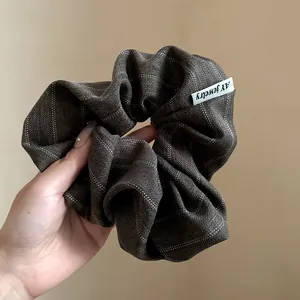Macro detail of a dark plaid vintage style fabric hair scrunchie held by hand