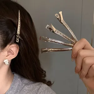 Close-up of minimalist silver metal duckbill hair clips shown on hair and in hand