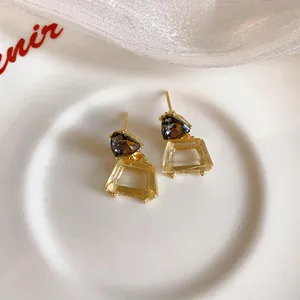 Nahaufnahme von goldfarbenen trapezförmigen Ohrringen mit dunkelgrauen Steinen auf einem Teller.