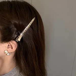 Detailed side view of a minimalist golden metallic duckbill hair clip on dark brown hair