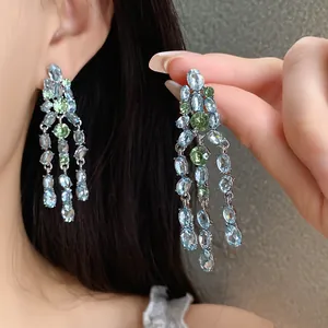 Close-up of sparkling blue and green oval zircon tassel earrings with silver needles.