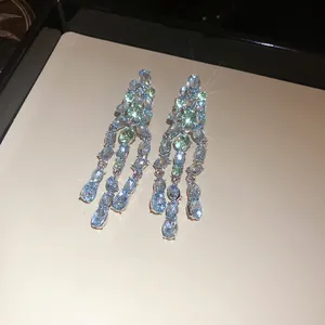 Close-up detail of silver tassel earrings with blue and green oval sparkling zircons.