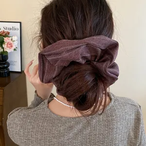 Back view of a messy bun hairstyle styled with a large striped brown fabric scrunchie