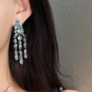 Close-up detail of luxury light blue and green zirconia tassel earrings worn by a model