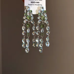 Detailed macro view of silver tassel drop earrings featuring green and clear oval zircon stones