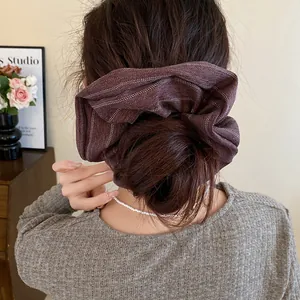 Detail view of a large burgundy striped fabric scrunchie worn on a woman's hair bun