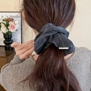 Detailed view of a dark grey pinstripe fabric scrunchie worn in an elegant ponytail