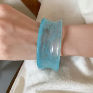 Macro detail of translucent light blue acrylic marbled wide bangle on woman's wrist