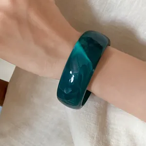 Detail view of a dark teal marbled acrylic wide bangle worn on a wrist with soft lighting