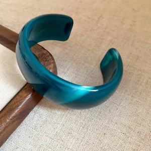 Detailed close-up of a marbled teal acrylic open cuff bracelet featuring a glossy finish