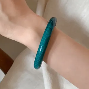 Detail view of dark green marbled acrylic bangle on wrist showing unique texture