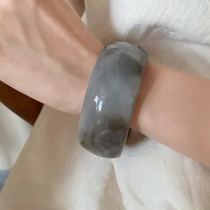 Elegant detail view of a wide gray marbled acrylic open bangle on a model's wrist