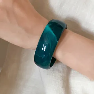 Macro view of a minimalist deep green marbled acrylic bangle worn on a wrist for elegant detail