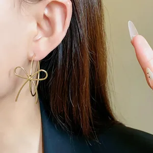 Macro detail of elegant golden metal bow hoop earrings worn by a model with dark hair