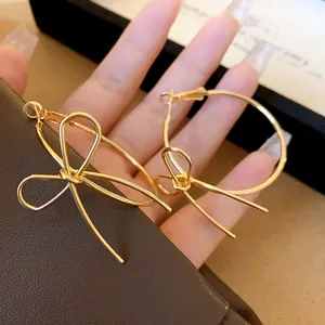 Detailed view of gold-toned bow hoop earrings held by hand, elegant jewelry design.
