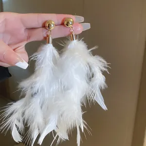 Close-up detail of white fluffy feather tassel earrings with golden ball studs