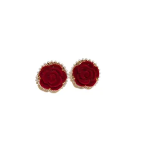 Elegant red velvet rose stud earrings with pearl halo on white background.