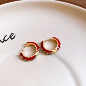 Macro detail of red and blue enamel gold hoop earrings on a beige ceramic plate