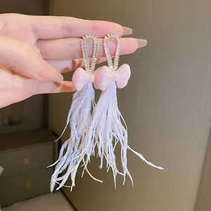 Detailed view of silver needle bow earrings with elegant long white feather tassels.