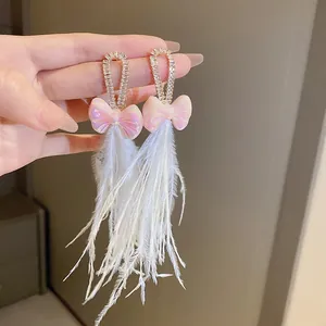 Macro view of elegant Bohemian rhinestone bow earrings with long white feather tassels.