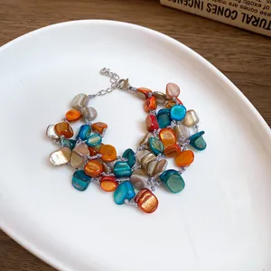 Macro detail showing colorful irregular shell fragments and stainless steel chain on a multilayered bracelet