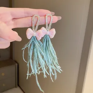 Detailed close-up of bow earrings with light green feather tassels and rhinestones