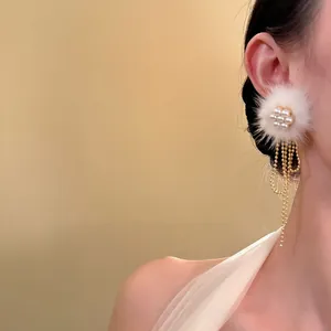 Nahaufnahme eines weißen Pelzball-Ohrrings mit Perlenblume und goldenen Quasten-Details
