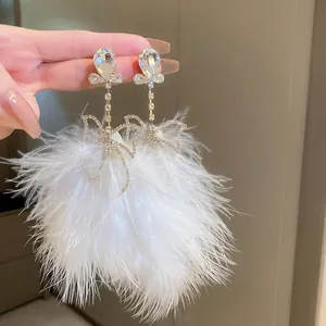 Detailed close-up of elegant white feather tassel earrings featuring rhinestone bow accents