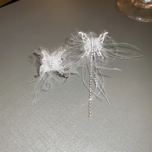 Close-up of bohemian butterfly earrings with white feathers and rhinestone tassels.