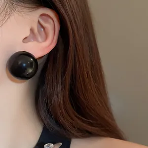 Close-up detail of oversized glossy black spherical stud earring worn on model's ear
