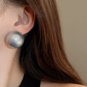 Close-up view of an oversized silver metallic ball stud earring worn on a model's ear