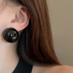 Detailed close-up of an oversized glossy black spherical stud earring worn on model's ear
