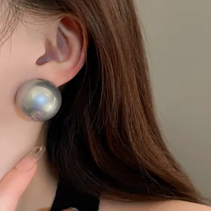 Elegant macro view of a large silver round pearl-like stud earring on a female model
