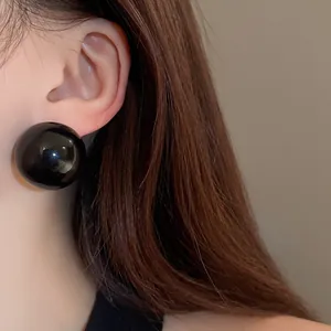 Close-up view of an oversized glossy black spherical stud earring on a model's ear