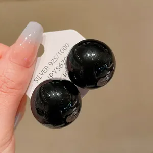 Close-up detail of oversized glossy black round stud earrings with silver needles