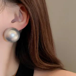Detailed close-up view of oversized silver pearl-style round stud earrings worn on the ear