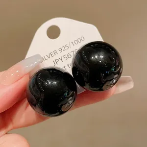 Detailed macro view of glossy oversized black spherical stud earrings on display card