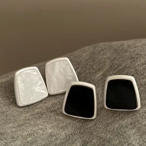 Close-up detail of minimalist black and white trapezoid resin stud earrings with silver frames