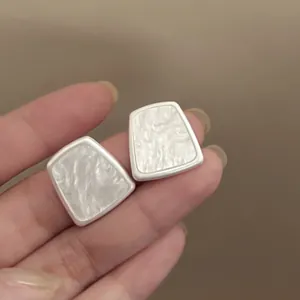 Close-up of minimalist trapezoid resin stud earrings with pearly texture and silver edges
