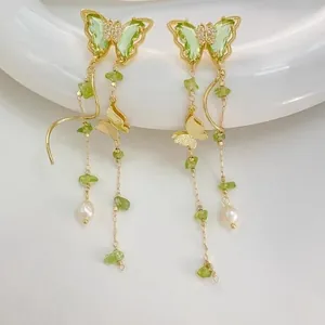 Elegant gold-toned butterfly tassel earrings with green stones and pearls, lifestyle view.